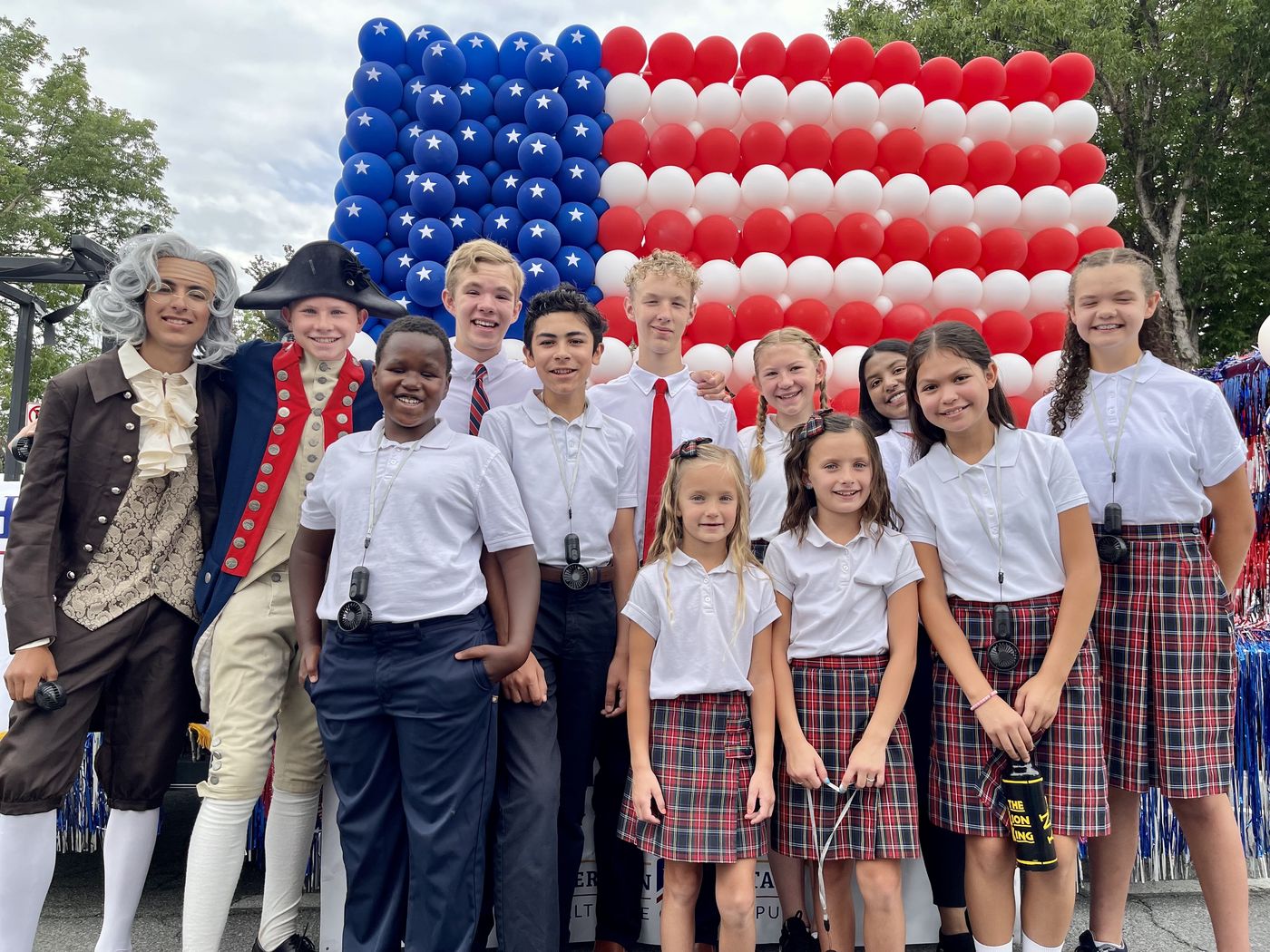 American Heritage School students, two dressed as Founding Fathers, in front of a balloon American flag at the Days of '47 parade