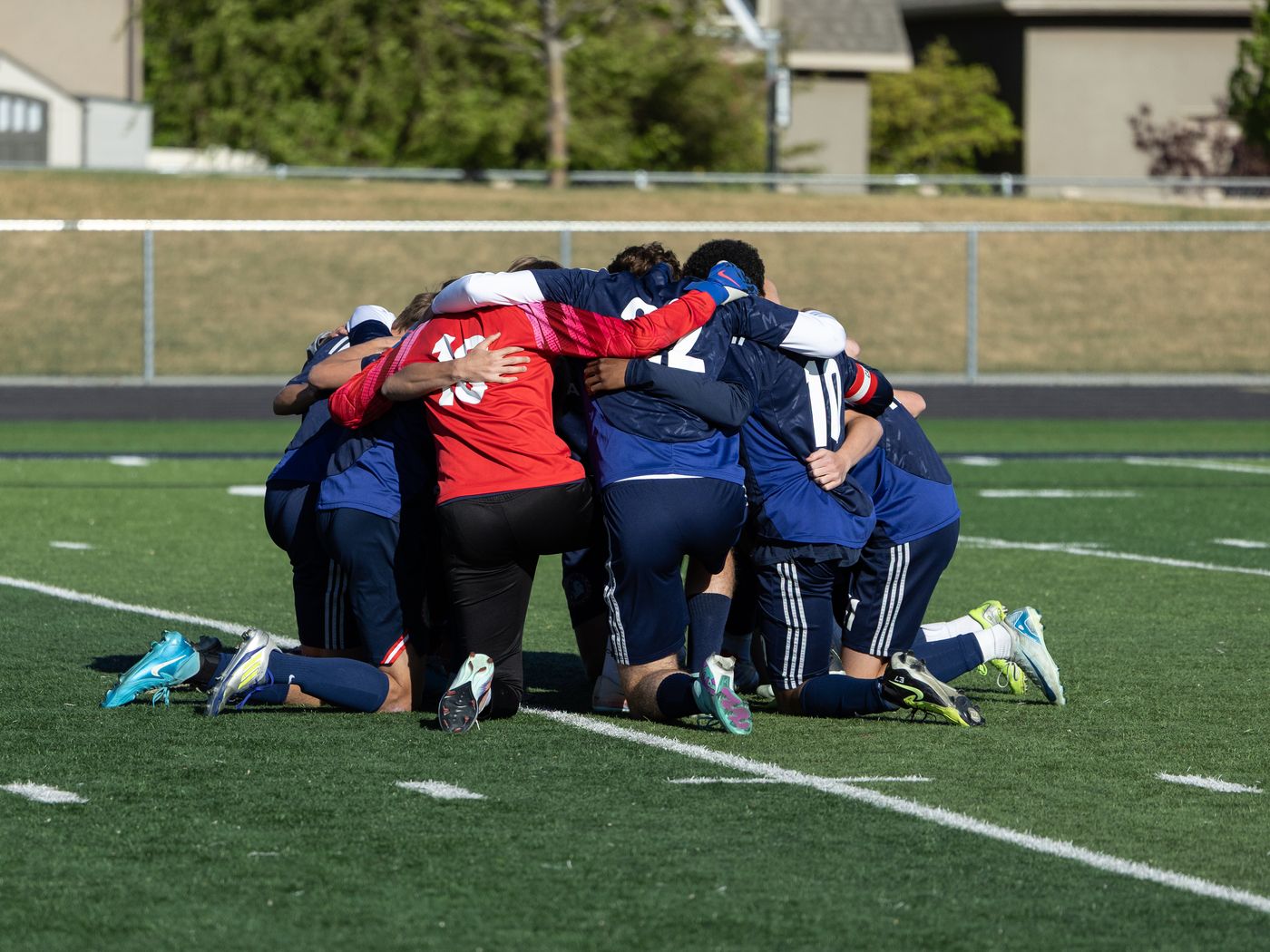 The American Heritage School boys soccer team kneeling together in prayer on the field before a game